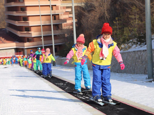 Một nhóm khá đông các trẻ em tham gia lớp trượt tuyết đứng trên một băng chuyền đặc biệt để lên sườn dốc.