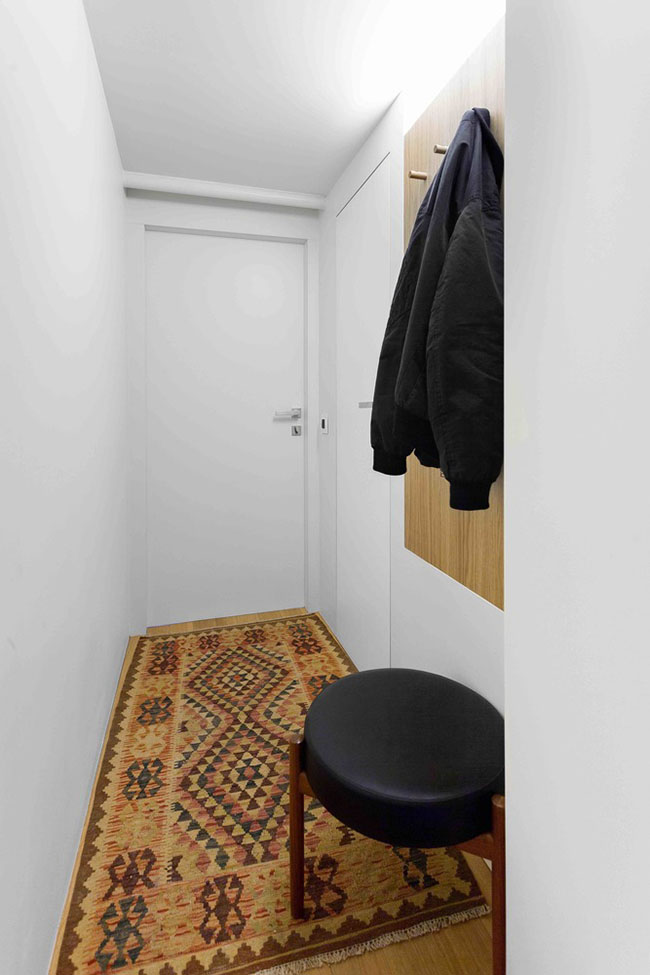 Ngay cửa ra vào của căn hộ được bài trí một tấm thảm màu sắc sặc sỡ nhằm mang lại không khí vui vẻ và cảm giác ấm áp cho căn hộ. Bức tường dọc hành lang vào căn hộ được biến tấu thành nơi treo áo khoác.