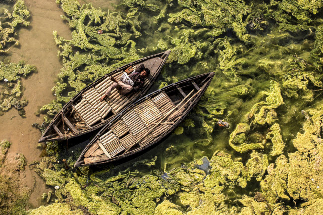 Người chèo thuyền nằm nghỉ ngơi và đọc báo trên thuyền ở Jamalpur, West Bengal, Ấn Độ. Ảnh: Debashis Mukherjee