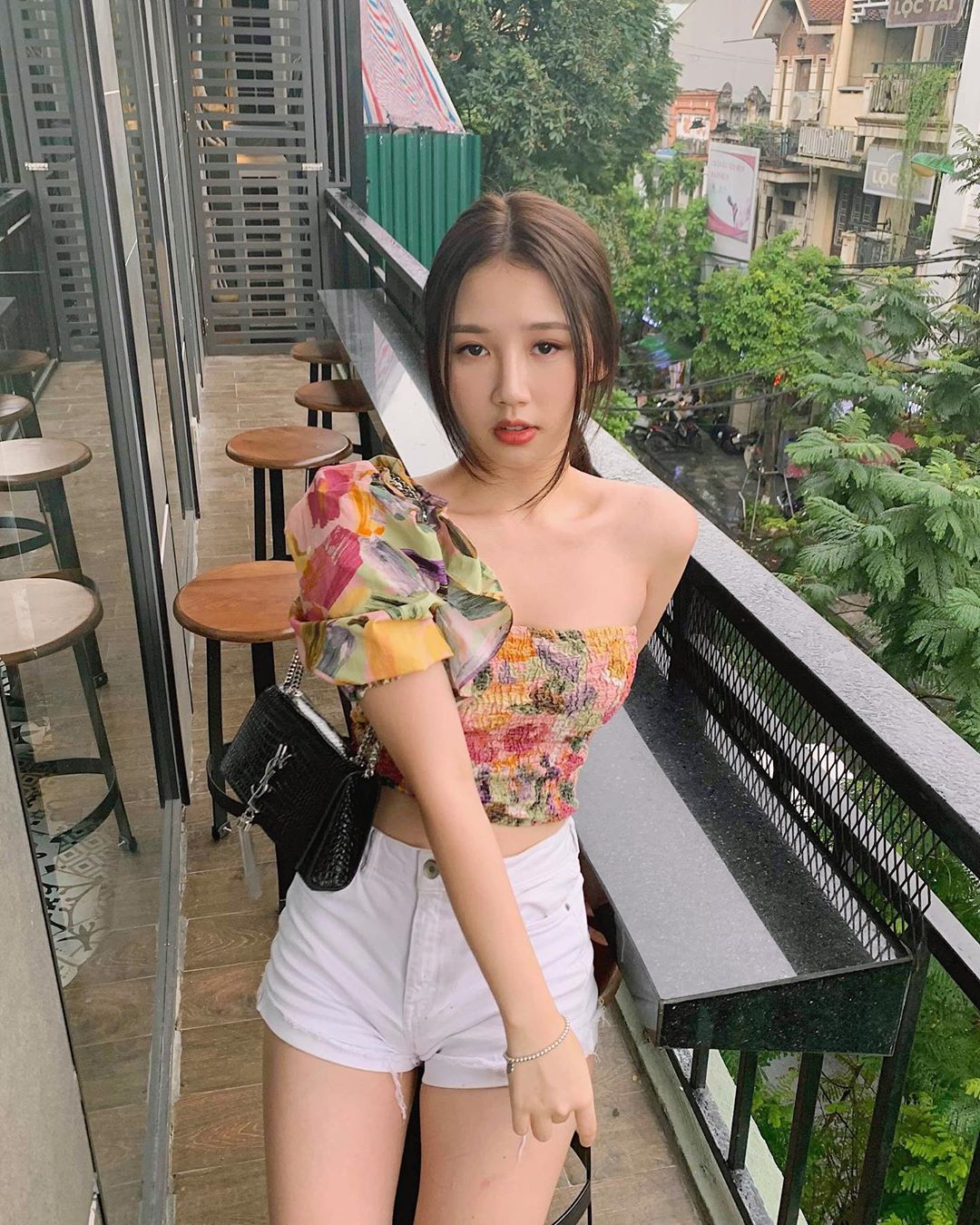 Amee chọn phối áo croptop họa tiết&nbsp;hoa may bằng voan nhẹ nhàng kiểu dáng lệch vai cùng quần short trẻ trung. Cô kết hợp với trang phục thêm&nbsp;chiếc túi xách màu đen của thương hiệu YSL.