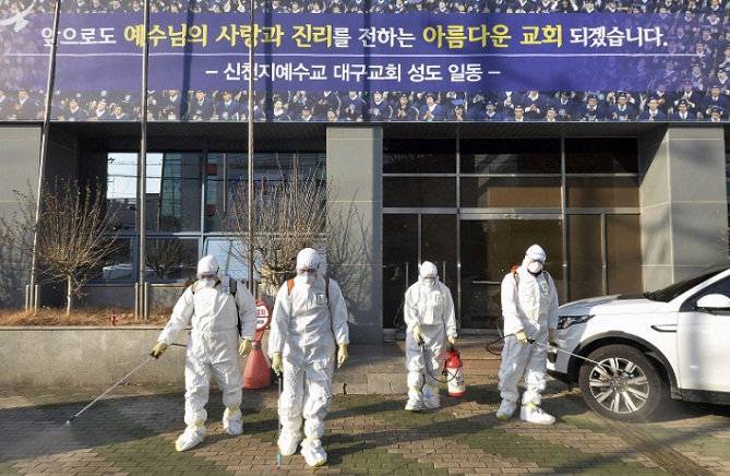 Các nhân viên y tế Han Quốc khử trùng trước cửa một nhà thờ ở thành phố Daegu.