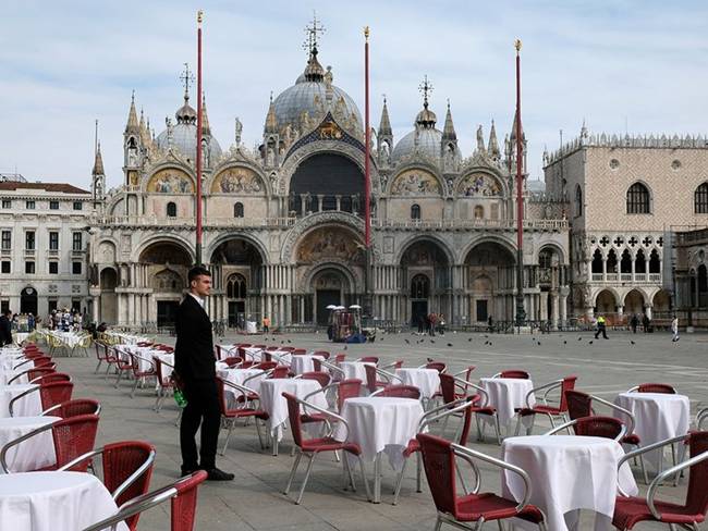 Một nhân viên phục vụ đứng cạnh những chiếc bàn không có ai ngồi tại nhà hàng ở Venice, Italia.