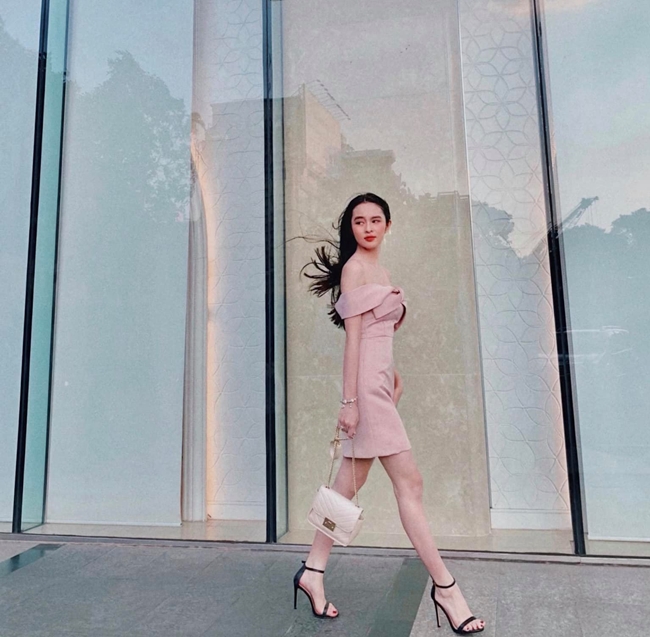Hoa khôi Đại học Tôn Đức Thắng trưởng thành trong bộ váy trễ vai màu hồng pastel. Phối cùng trang phục cô chọn đi giày cao gót màu đen và xách túi màu trắng.