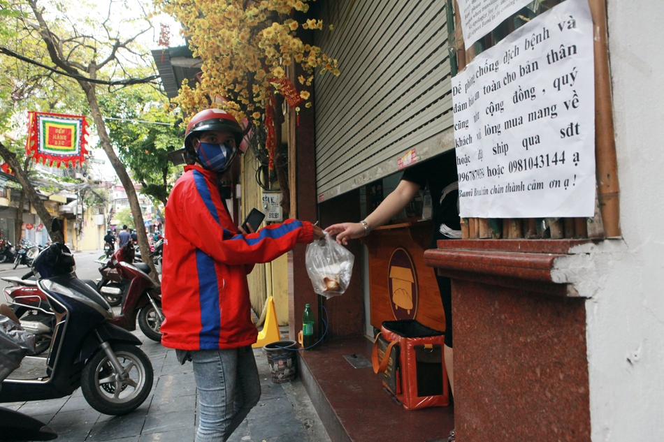 Những quán mở cửa bán hàng đều treo biển ghi “Để phòng chống dịch và an toàn cho bản thân cũng như cộng đồng. Quý&nbsp;khách vui lòng mang về hay hoặc ship qua số điện thoại”. Hình ảnh quán bán bánh mì trên phố Hàng Bạc (quận Hoàn Kiếm) - shipper (người giao hàng) luôn tất bật lấy đồ ăn để giao cho khách.