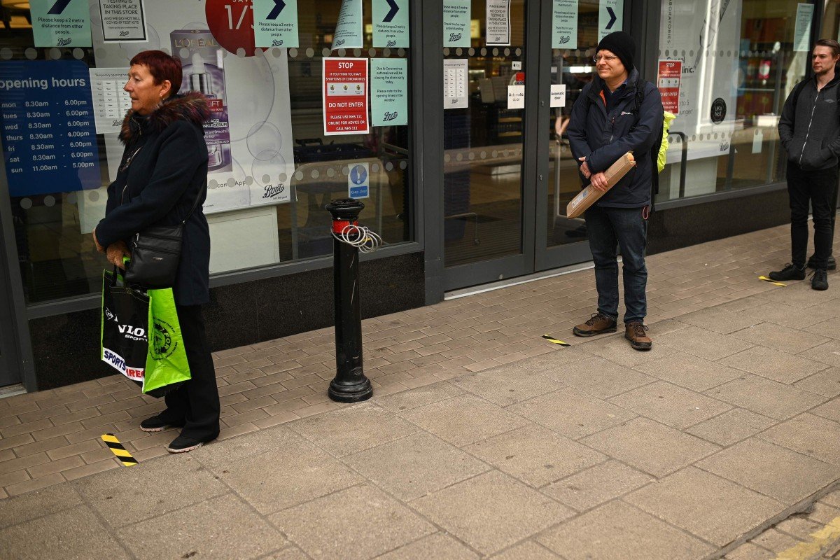 Người dân Anh tuân thủ quy định giữ khoảng cách khi chờ đến lượt mua sắm.
