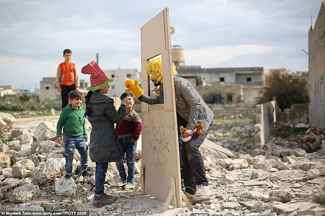 Mouneb Taim, người Syria đã chụp bức ảnh ấm lòng nhưng cũng đau lòng này ở Saraquib, Syria. Một người đàn ông biểu diễn múa rối cho trẻ em xem, nơi xảy ra các cuộc bạo động và bị tàn phá bởi chiến tranh.
