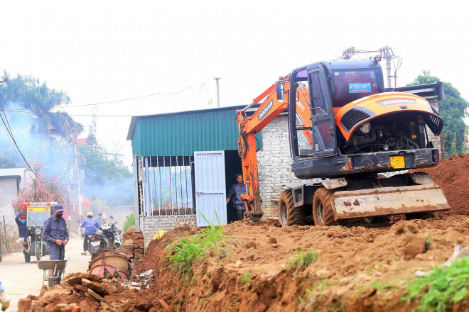 Một nông dân đang dùng máy xúc, máy ủi để san lấp lại ruộng đào sau một năm canh tác.