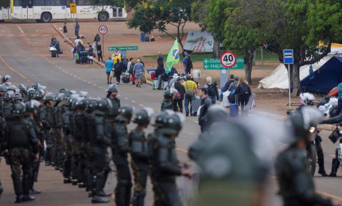 Cảnh sát chống bạo động Brazil giám sát người ủng hộ ông Bolsonaro rời khu trại ở Brasilia hôm 9-1. Ảnh: Reuters