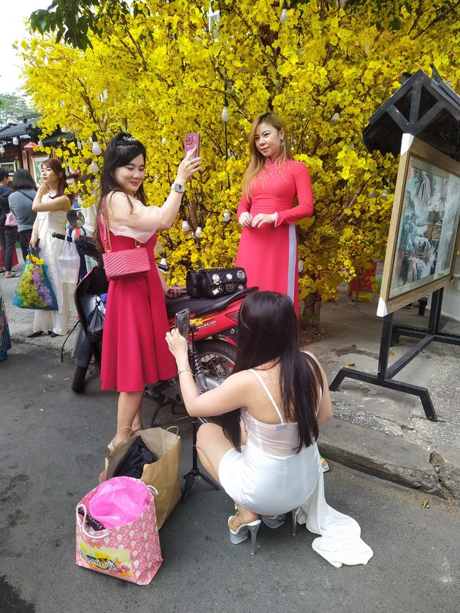 Một nhóm các bạn nữ mang theo nhiều trang phục và điện thoại, vừa quay phim vừa chụp ảnh cho nhau, không quan tâm đến các "phó nháy" ở lễ hội Tết.