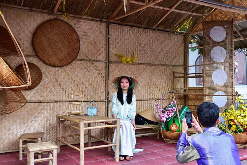 Một ngôi nhà tranh của miền quê với bàn ghế cho khách tham quan, tạo dáng chụp ảnh bên đường phố đông đúc.