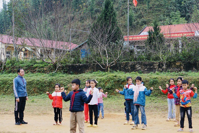 Các em học sinh Trường phổ thông Cao Sơn (tại bản Son Bá Mười) đang học thể dục phía trước những cây đào khoe sắc thắm