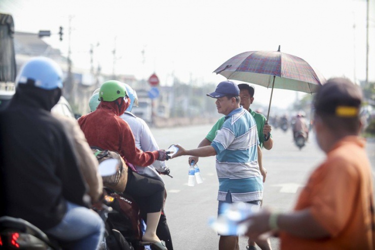 Ông Hòa trao những chai nước suối cho người đi đường về quê đón Tết trong thời tiết nắng gắt trưa 5-2. Ảnh: HD