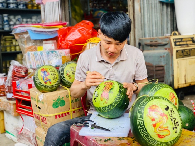 Mặc dòng người xe hối hả ken dày bên ngoài đường nhưng anh Phạm Quang Thiếu (29 tuổi, trú huyện Hương Sơn, tỉnh Hà Tĩnh) vẫn lặng lẽ với công việc của mình là "trang điểm" cho quả dưa hấu. Trong ảnh những con rồng vàng mãnh dũng được tạo hình lên quả dưa rất tinh tế, đẹp mắt thu hút khách trong dịp Tết năm nay.