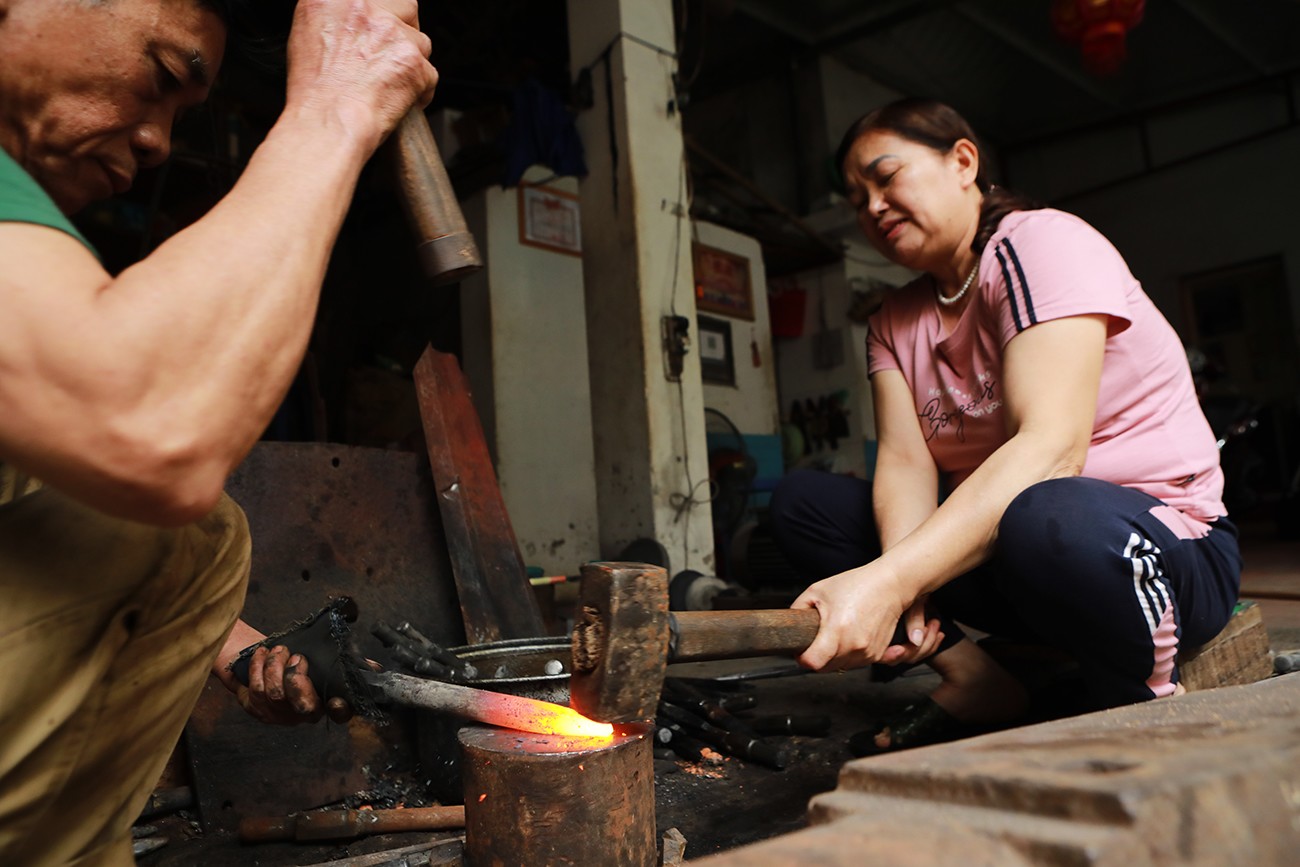 Nghệ nhân Hoàng Văn Cung (64 tuổi) và vợ là bà Hoàng Thị Hà miệt mài với công việc rèn thủ công bên lò than nóng rực. “Tôi là người làng nghề khác về làm dâu ở làng rèn này. Tôi phụ việc cho chồng từ công việc đơn giản đến công việc nặng nhọc như quai búa. Tuy vất vả nhưng mình tự nguyện gắn bó với đe, búa, lò lửa nên mọi sự vất vả cũng cảm thấy bình thường”, bà Hà nói.