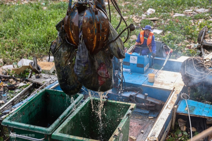 Ông Nguyễn Xuân Sơn lái thuyền vớt rác bỏ vào thùng. Một số loại như túi nilon, nệm thấm nước khá trơn trượt nên phải cạp nhiều lần mới vớt lên được. 
