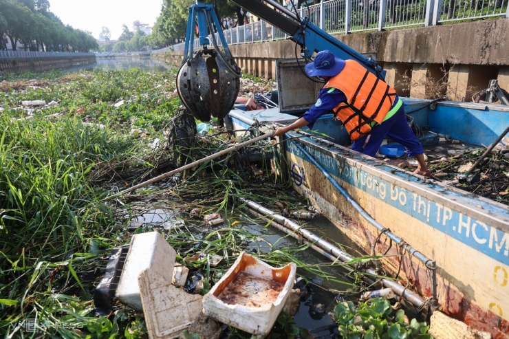 Anh Thanh Sơn, 47 tuổi dùng cào kéo cỏ, lục bình, rác lại để dễ vớt.