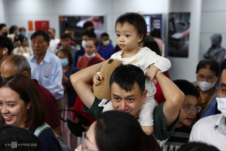 Bé Quỳnh Anh, 2 tuổi được cha công kênh trên vai. Nhiều trẻ em mệt mỏi, ngồi bệt xuống sàn vì phải chờ đợi lâu.