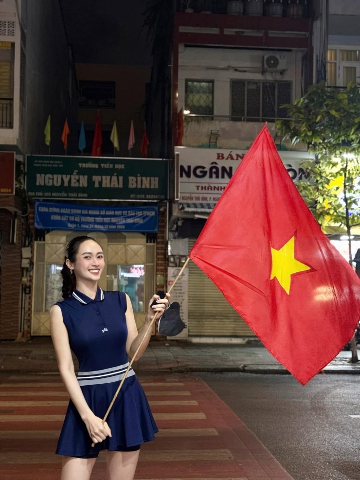 Á hậu Miss Universe Vietnam 2024 Vũ Thúy Quỳnh cầm cờ đỏ sao vàng, cổ vũ dòng người "đi bão" sau chiến thắng của đội tuyển Việt Nam.