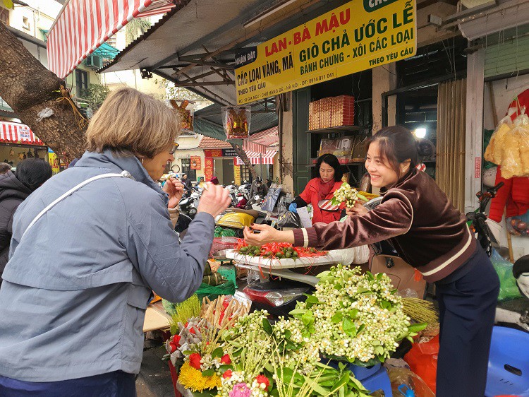 Một số khách nước ngoài&nbsp;thích thú với những bông hoa bưởi trắng có mùi thơm dễ chịu được bày bán tại phố Hàng Bè.