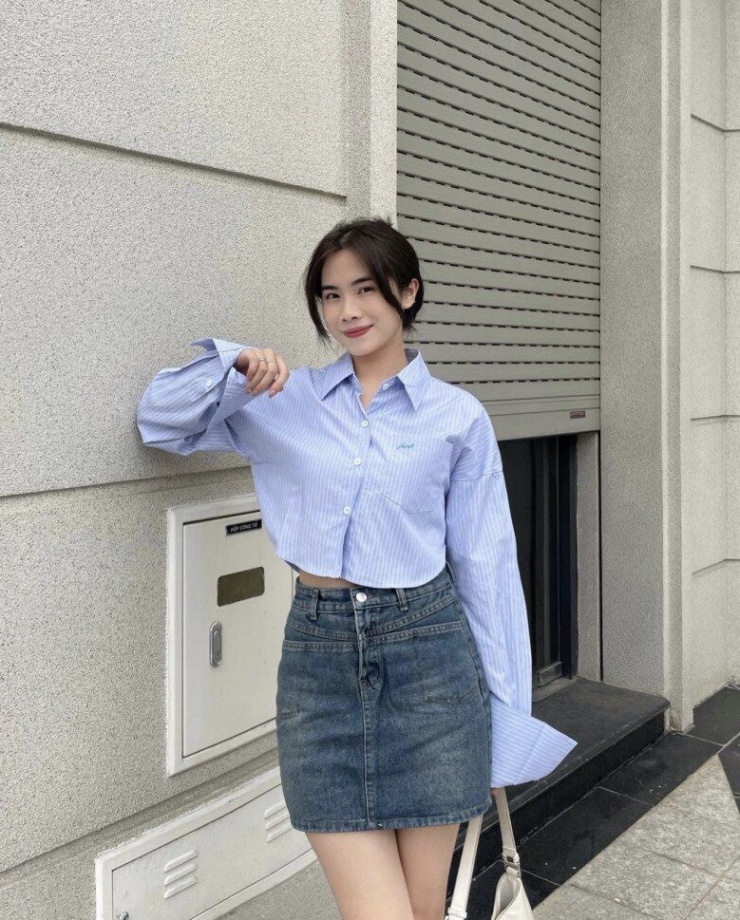 Một sự kết hợp tinh tế giữa sơ mi croptop kẻ sọc và chân váy denim, tạo nên vẻ ngoài vừa thanh lịch vừa phóng khoáng. Thiết kế tay áo rộng, buông nhẹ cùng đường sọc xanh pastel giúp tổng thể trông nhẹ nhàng nhưng vẫn nổi bật.