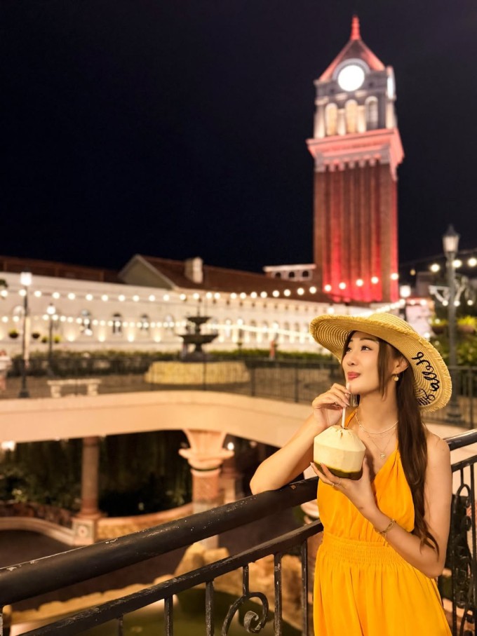 Chu Trí Hiền đứng tại thị trấn Hoàng Hôn (Sunset Town) ở An Thới, tạo dáng trong khu quảng trường, cạnh tháp đồng hồ phong cách châu Âu. Khu vực lấy cảm hứng từ kiến trúc Địa Trung Hải, ban đêm lên đèn rực rỡ.