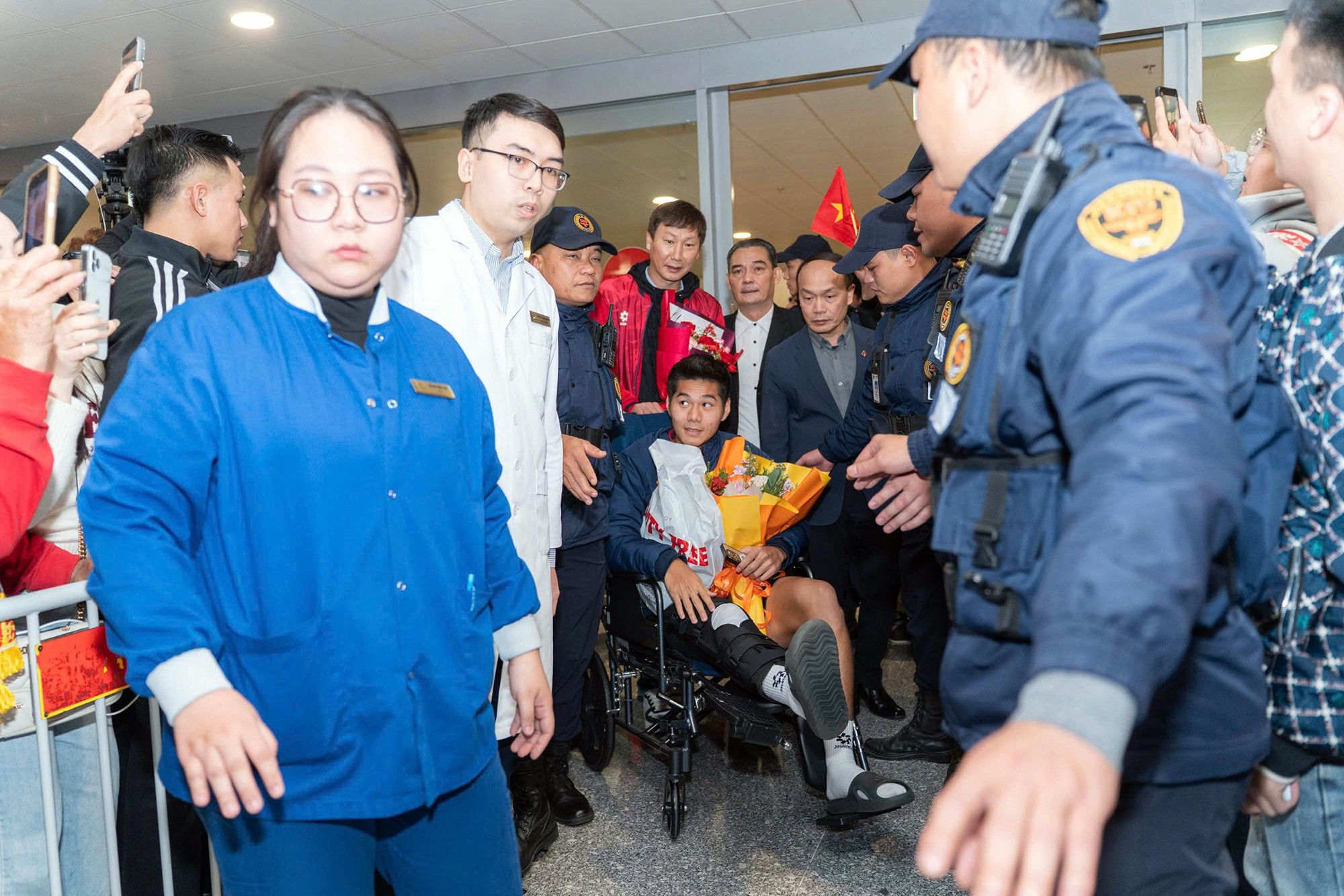 Hiểu Minh ngồi xe lăn, được HLV Kim Sang Sik và đội trưởng Khuất Văn Khang đẩy ra. VFF cũng chuẩn bị xe chuyên dụng và bác sĩ để chăm sóc Hiểu Minh ngay từ khi trung vệ này đặt chân về đến Nội Bài.