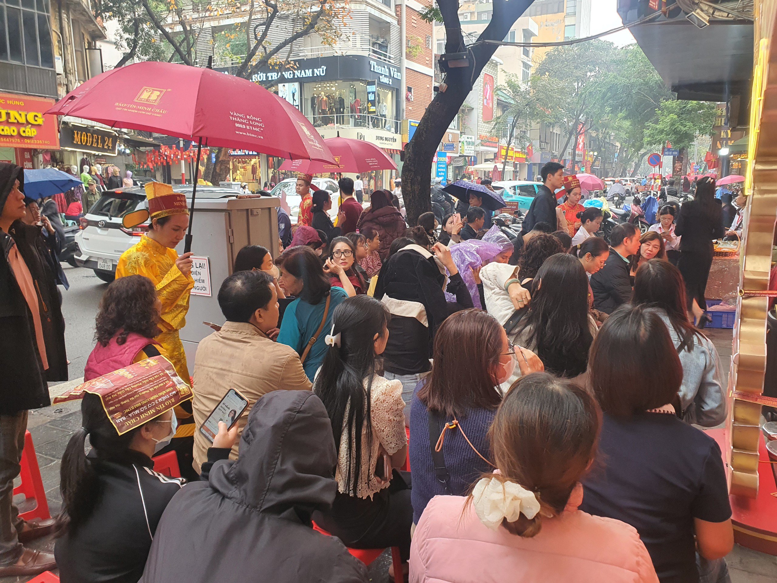 Mặc dù thời tiết hôm nay có mưa nhỏ nhưng hàng trăm người vẫn ngồi thành hàng chờ vào mua vàng trong ngày vía Thần Tài để lấy may.