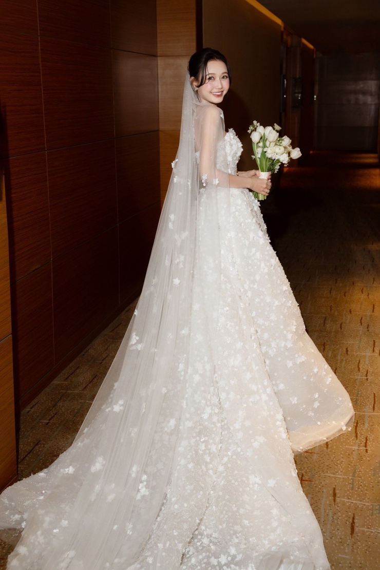 Trên thân váy phủ kín hơn 3.000 bông hoa 3D đính kết thủ công từ organza và tulle, tạo nên bề mặt sống động.