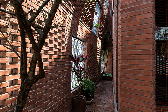 Căn nhà được bao bọc bởi hai lớp tường gạch cách nhau một hành lang nhỏ với cây xanh dọc lối đi.