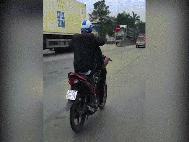 Nam thanh niên dùng 2 chân điều khiển xe máy, tay cầm điện thoại trên quốc lộ