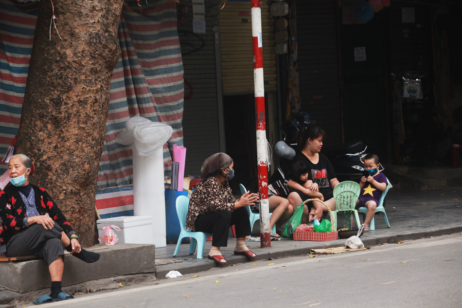 Một người phụ nữ ngồi bên các con, bày bán chân gà nướng trên phố Hàng Mã mà không đeo khẩu trang.