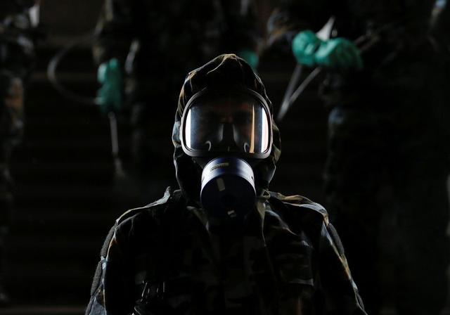 Một binh sĩ đeo mặt nạ phòng độc đang phun thuốc khử trùng vào ban đêm (ảnh: Reuters)