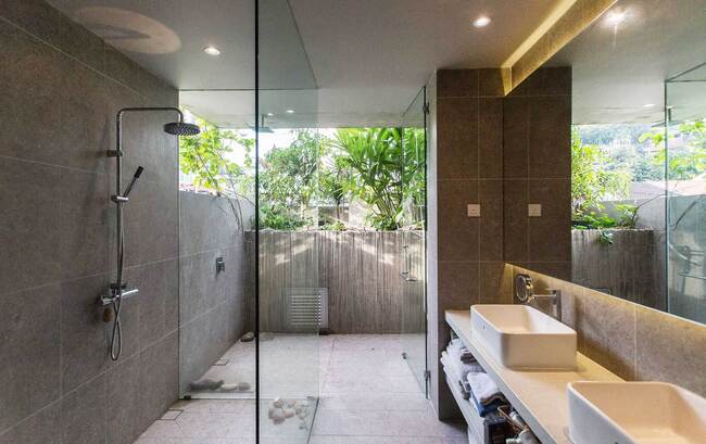 Phòng tắm rộng lớn, hiện đại với những tấm kính lớn gần những bụi cây xanh.
