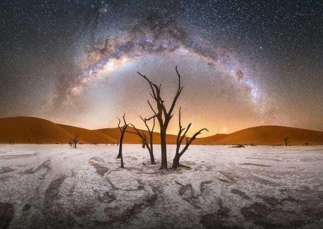 1. Bức ảnh "Deadvlei" của nhiếp ảnh gia Stefan Liebermann cho thấy Dải Ngân hà trải dài trên bầu trời tại Công viên Quốc gia Namib-Naukluft ở Namibia. Liebermann viết:"Những cái cây ở Deadvlei đã chết hơn 500 năm. Nằm trong Công viên Namib-Naukluft ở Namibia, những cây non này đã lớn lên nhờ các con sông địa phương đầy nước sau nhiều cơn mưa lớn. Nhưng chúng đã chết dần chết mòn sau khi sông cạn nước và cát xâm lấn chiếm đóng. Dải ngân hà của chúng ta tạo thành một vòm cung tuyệt đẹp bên trên thân cây lớn".