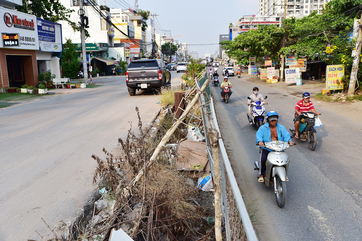 Một phần đoạn đường được nâng cao, trải thảm nhựa, phần còn lại vẫn chưa được thi công đang bị thấp đến nửa mét, ngăn cách bởi rào chắn chất đầy rác.