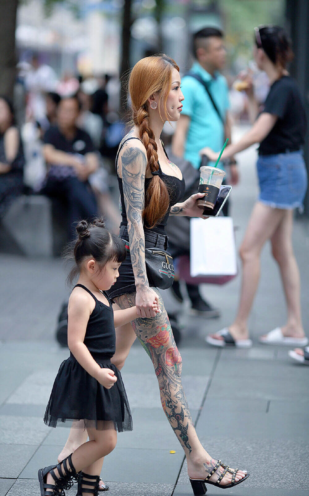 Mẹ trẻ dắt con nhỏ đi dạo phố trong bộ trang phục gây tranh cãi bao gồm áo 2 dây và quần short, tôn dáng tối đa.