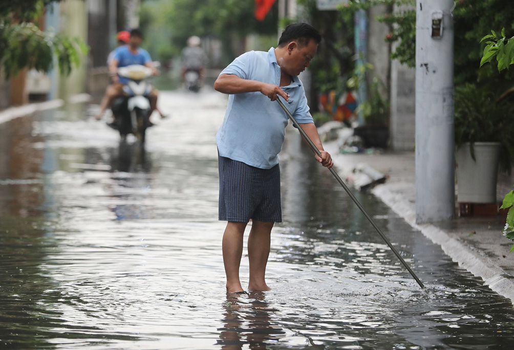 Ông Dũng&nbsp;phải khơi rác ở các cống trong hẻm để thoát nước nhanh hơn.