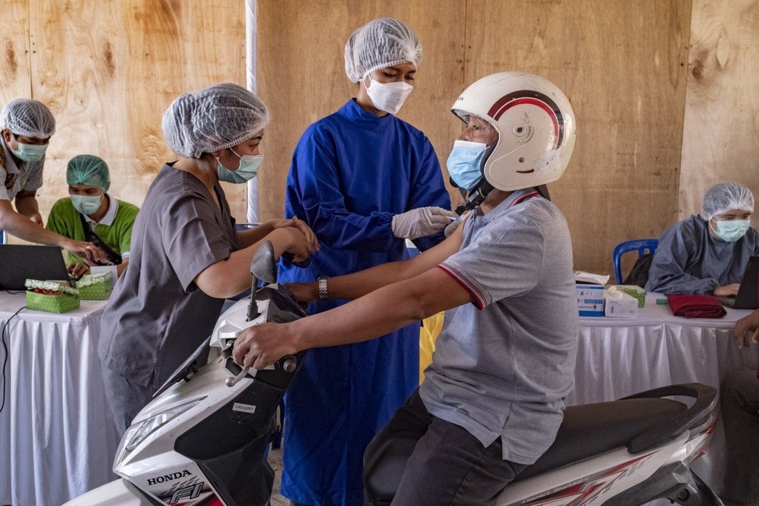 Một người đàn ông lái xe máy đến điểm tiêm chủng ở Indonesia.