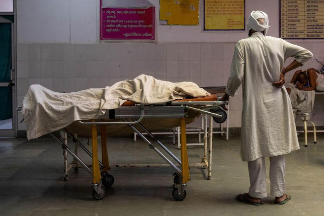 Một người đàn ông Ấn Độ đứng cạnh thi thể vợ qua đời vì COVID-19. Ảnh: Reuters