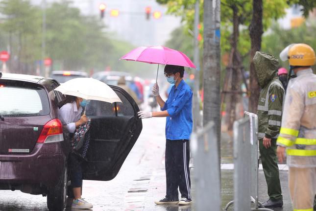 Một thí sinh được gia đình đưa đi thi bằng xe ô tô được thanh niên tình nguyện che chắn thêm ô cho khỏi ướt.