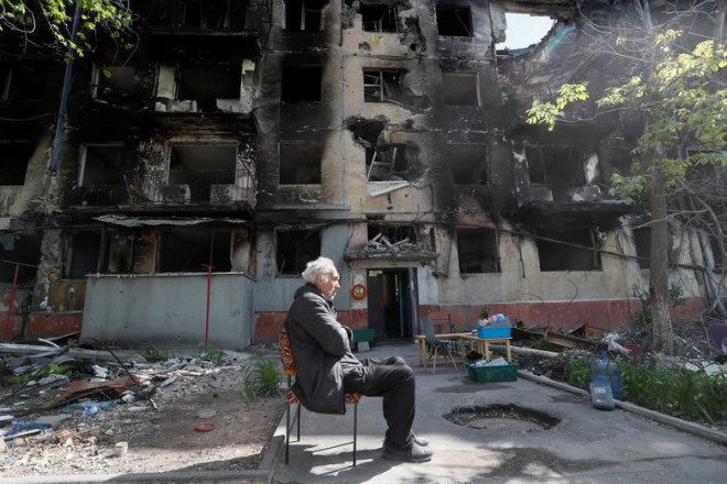 Một người dân địa phương ngồi trên sân gần một khu căn hộ bị hư hại nặng nề trong cuộc giao tranh Ukraine-Nga ở thành phố cảng phía Nam Mariupol, Ukraine ngày 20/5.