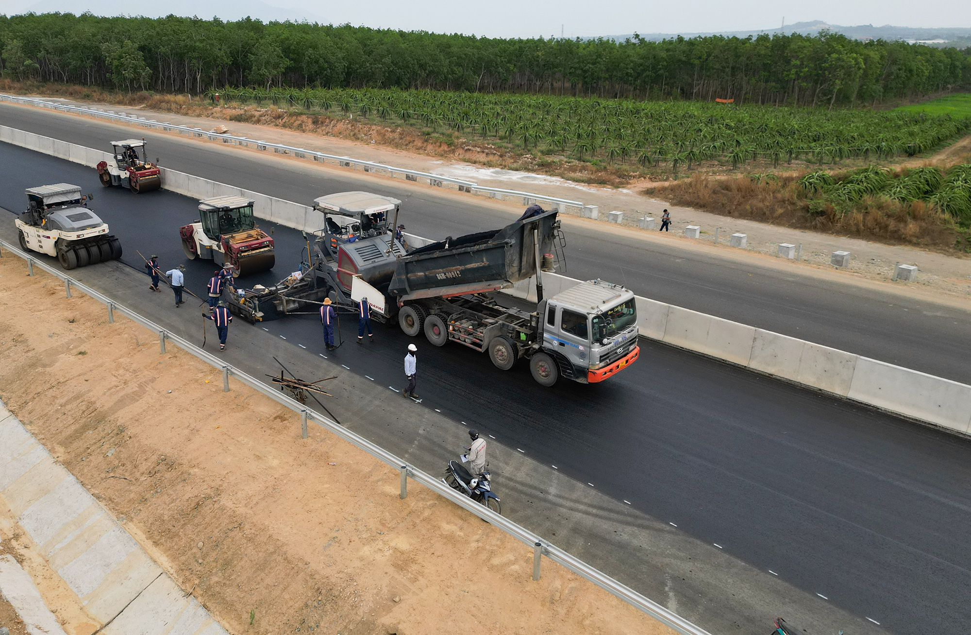 Trên một đoạn cao tốc qua địa bàn tỉnh Bình Thuận, hàng chục xe tải, máy thảm nhựa, xe lu nền đang gấp rút hoàn thành lớp thảm nhựa cuối cùng.