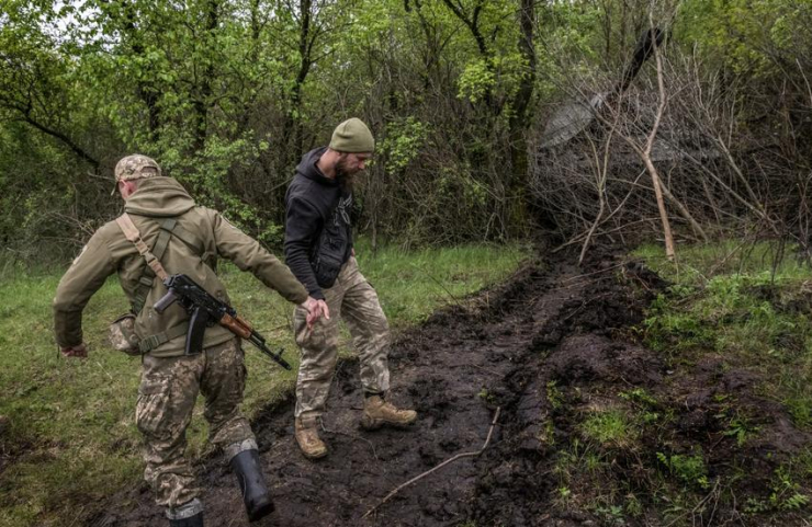 Lính Ukraine nắm tay nhau đi trên đoạn đường bùn đất. Ảnh: THE NEW YORK TIMES