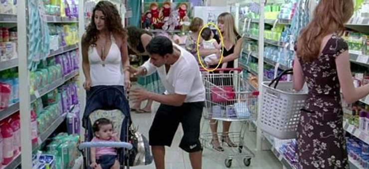 Trong cảnh quay này, em bé được mẹ ẵm trên tay đang mặc bộ đồ màu trắng.

