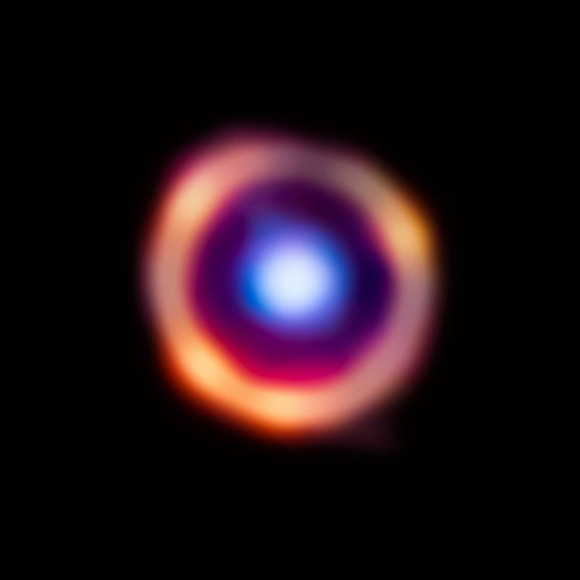 Thiên hà SPT0418-47 màu đỏ với các phân tử hữu cơ sáng lên dưới ánh sáng cam, trong khi một thiên hà tiền cảnh được đánh dấu bằng màu xanh - Ảnh: NASA/ESA/CSA