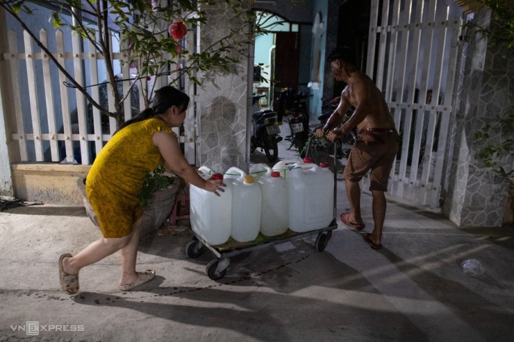 Gần 23h, ông Đoàn Dũng Tiến ở ấp 3, Tân Phước, cùng người thân kéo nước về nhà. "Nhà tôi có ba hộ phải lấy 20-30 can mới đủ dùng", người đàn ông 39 tuổi nói.