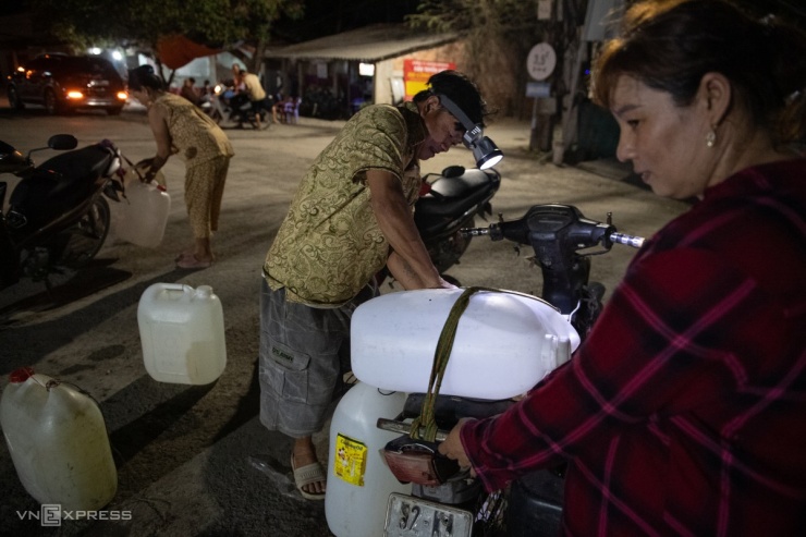 Trời tối, ông Huỳnh Văn Nghĩa dùng thêm đèn treo trên đầu để tiện lấy và chở nước.