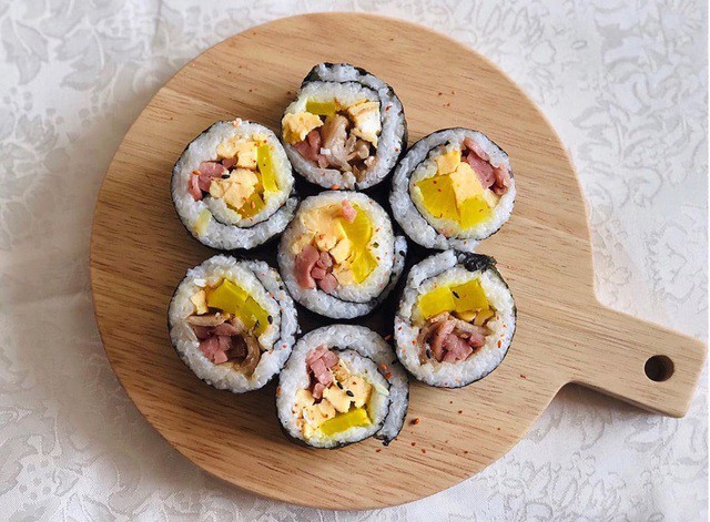 Kimbap là món cơm cuộn trong lá rong biển nổi tiếng xứ kim chi. Phần nhân kimbap bao gồm xúc xích, thanh cua, trứng rán, dưa leo, cà rốt. Các nguyên liệu được cắt thành thanh dài, dày khoảng 1 cm để dễ cuốn. Phần cơm được trộn cùng dầu mè để dậy mùi, thơm ngon hơn. Bạn trải đều cơm lên tấm rong biển, thêm các loại nhân và cuốn chặt tay để khi cắt, miếng cơm cuộn đẹp mắt. Ảnh: Munchiewingwing.