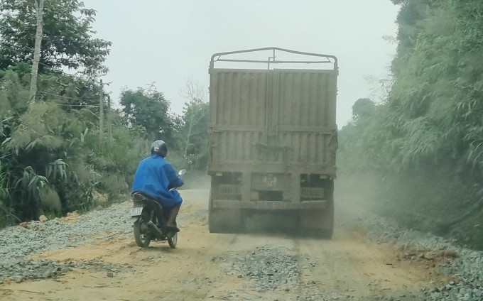 Người dân mặc áo mưa giữa trời nắng để tránh bụi khi đi trên quốc lộ 14D. Ảnh: Đắc Thành