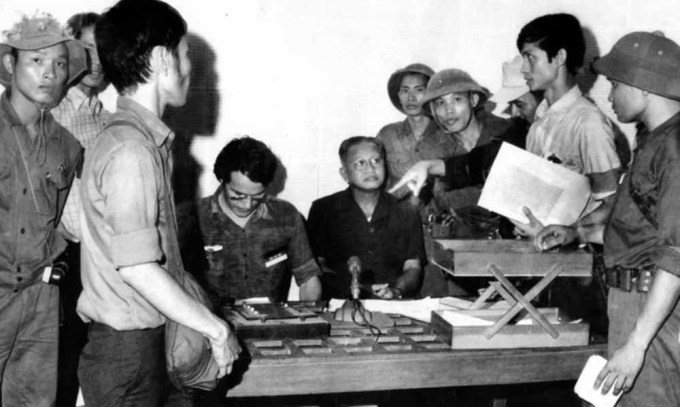 Tổng thống chính quyền Việt Nam Cộng hoà Dương Văn Minh (áo đen, ngồi) thời điểm đọc tuyên bố đầu hàng tại Đài Phát thanh Sài Gòn trưa 30/4/1975. Ảnh: Kỳ Nhân